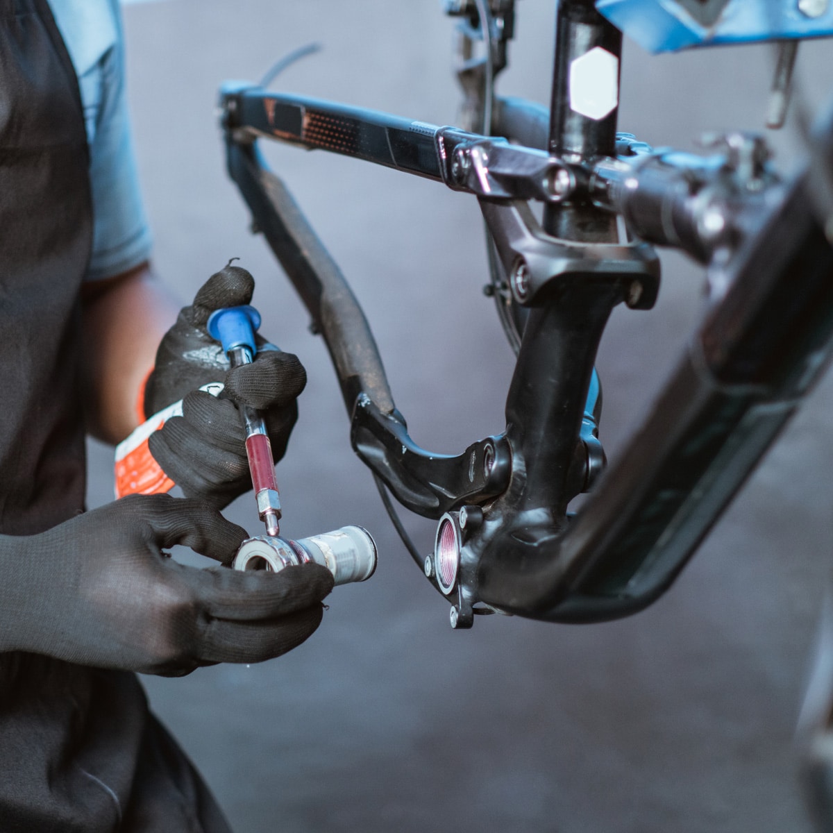 A person wearing black gloves uses a tool to work on a bicycle bottom bracket, with a partially visible bike frame in the background. The image conveys the concept of eliminating mechanical drag on a bicycle.