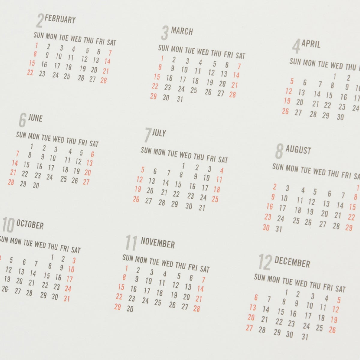A close-up of a minimal 2023 wall calendar symbolizing the concept of periodization in endurance sports, displaying all 12 months with Sundays highlighted in red and the remaining days in gray on a white background.