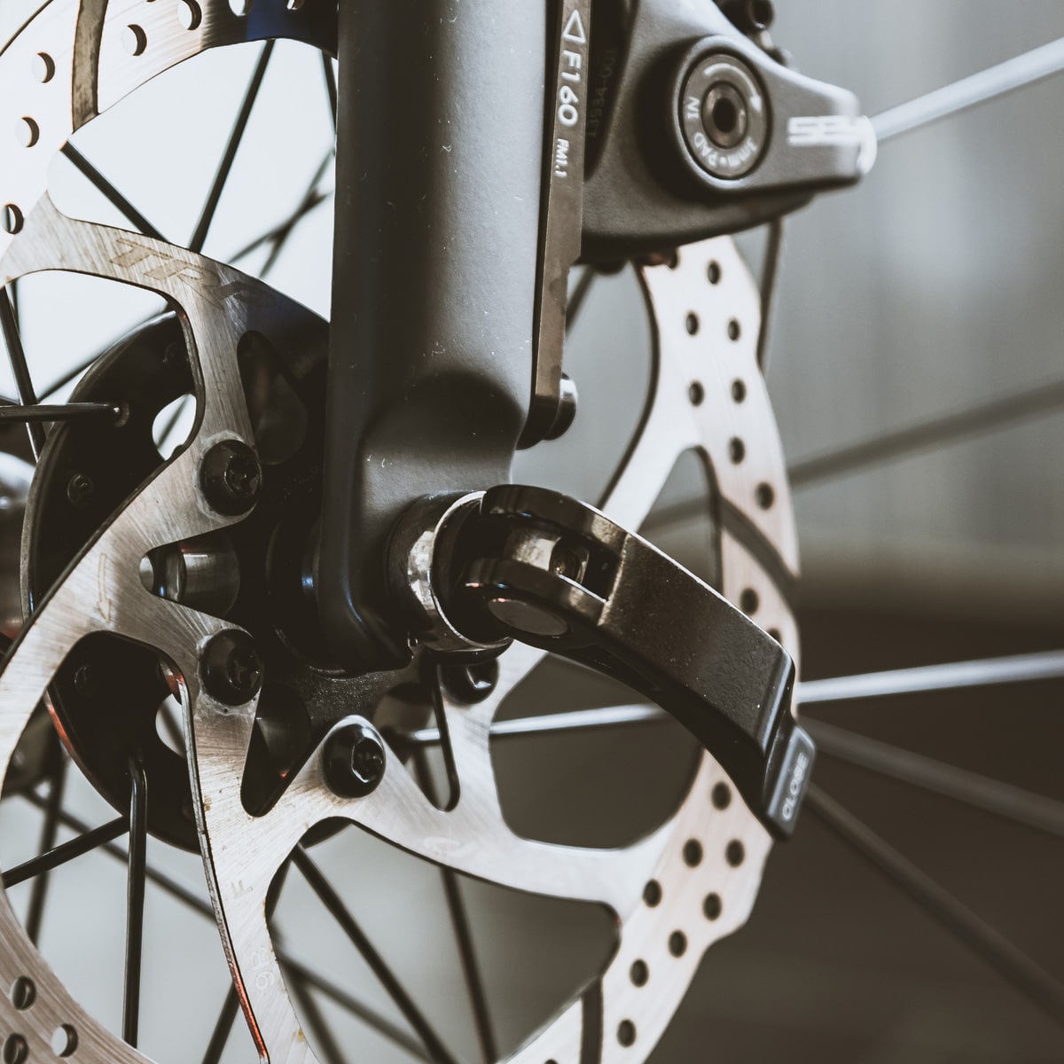 Close-up of a bicycle disc brake and caliper, featuring the metal rotor attached to the wheel and the black quick release skewer on the axle. The photo highlights precise mechanical details and key components.
