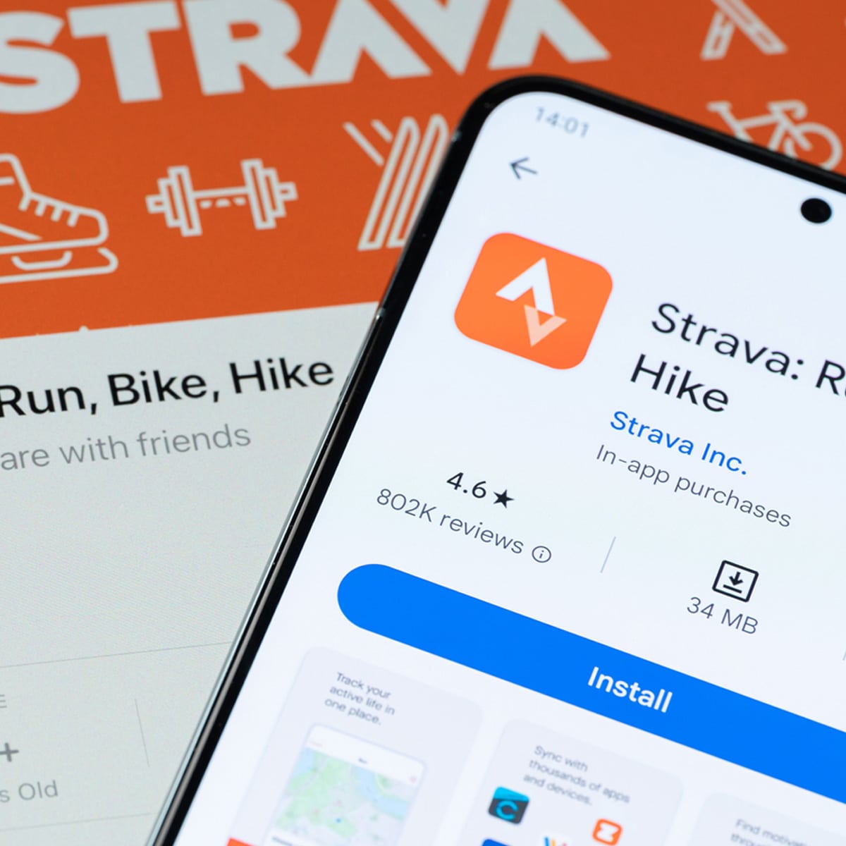 A smartphone displays the Strava app screen, showing its rating and reviews. In the background, a Strava promotional graphic with fitness icons and the Strava logo is partially visible.