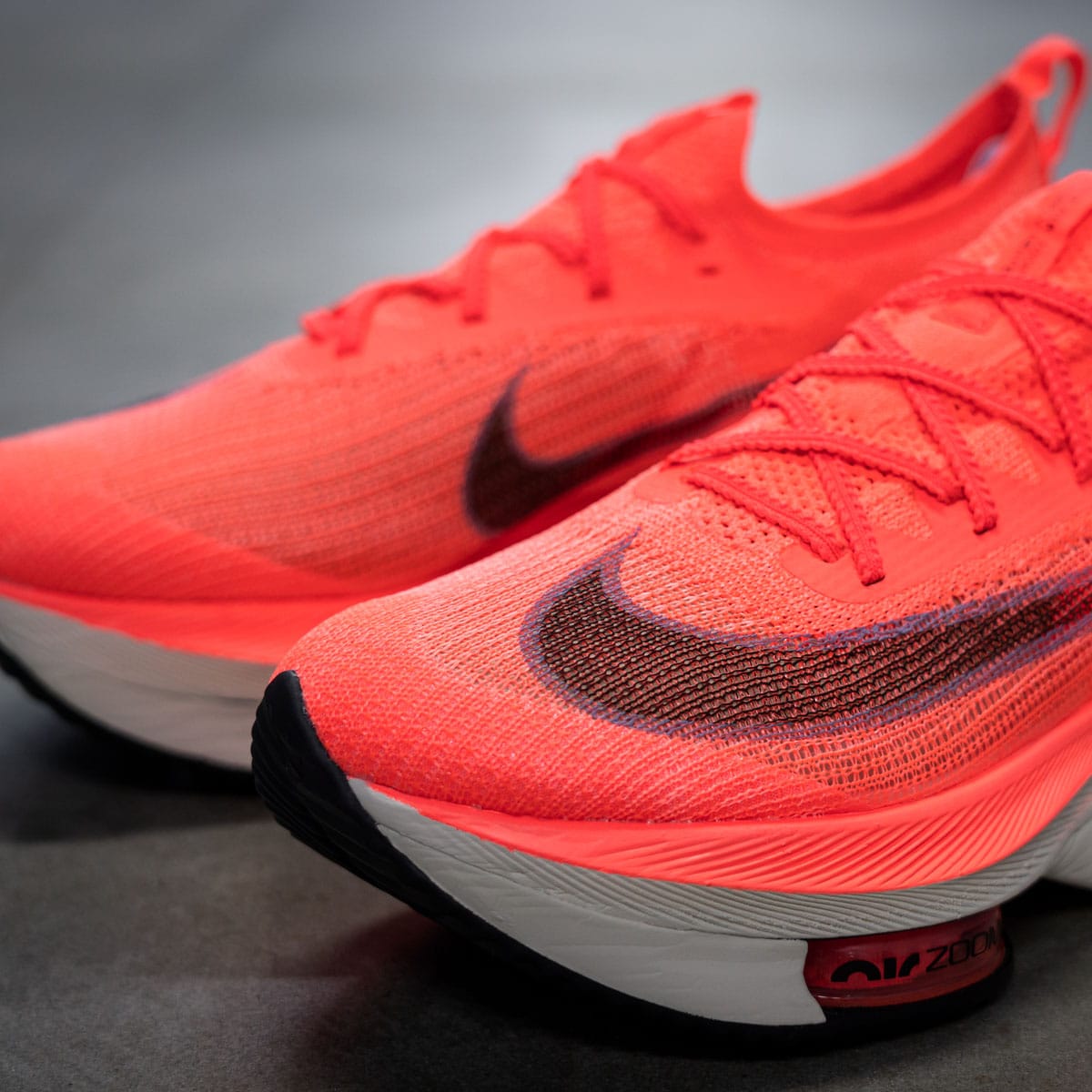 Close-up of bright orange running shoes with a black Nike swoosh, highlighting the breathable mesh upper.