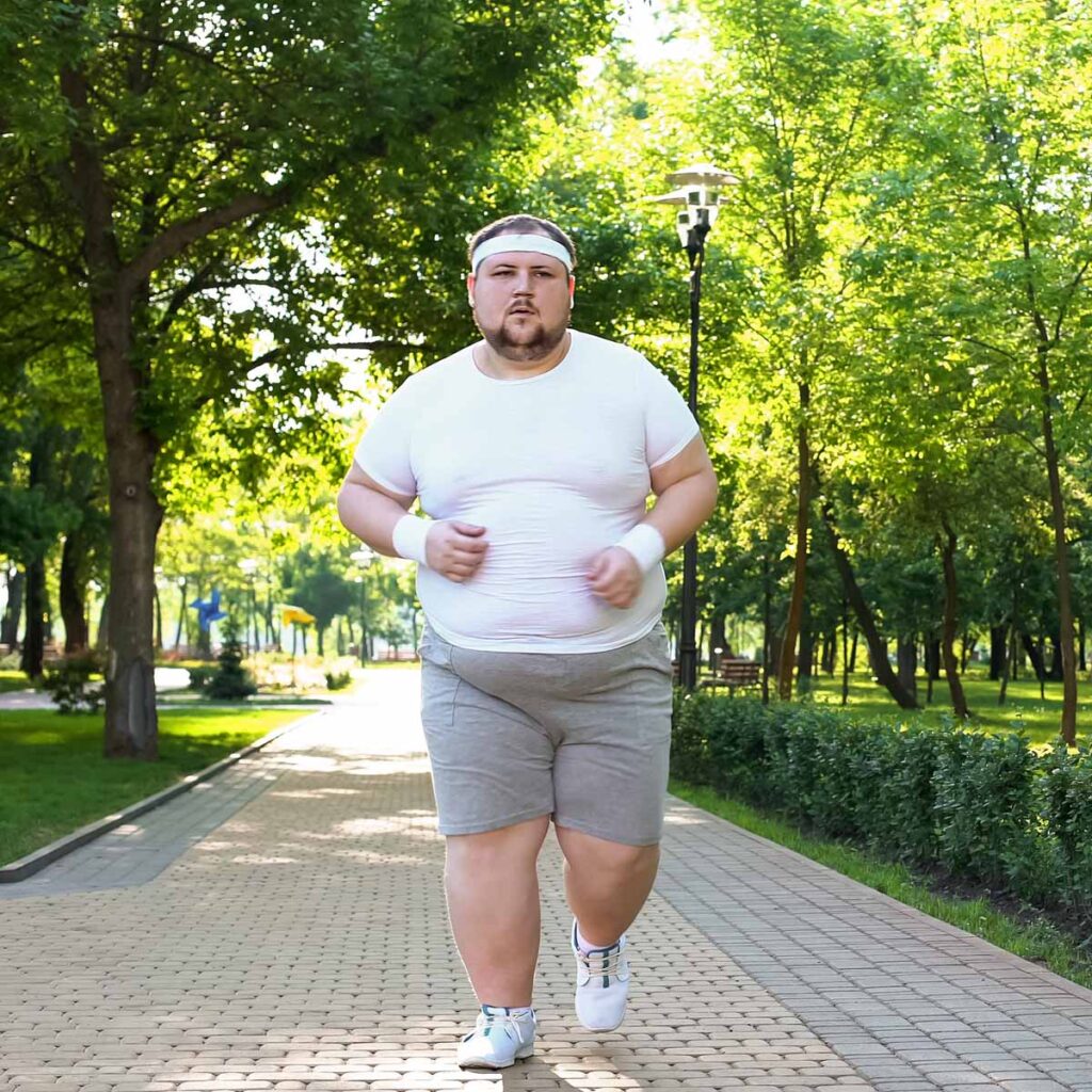 An overweight man in athletic wear jogs along a sunlit park path lined with green trees, symbolizing the concept of heart rate Zone Inflation in endurance sports.
