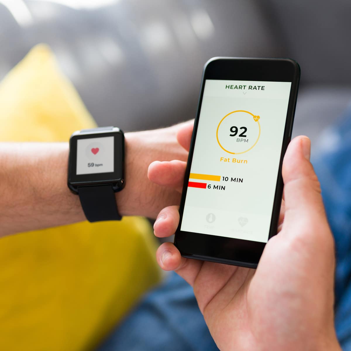 A person checks their heart rate on a smartwatch and smartphone, displaying 92 bpm and time in the Fat Burn zone.