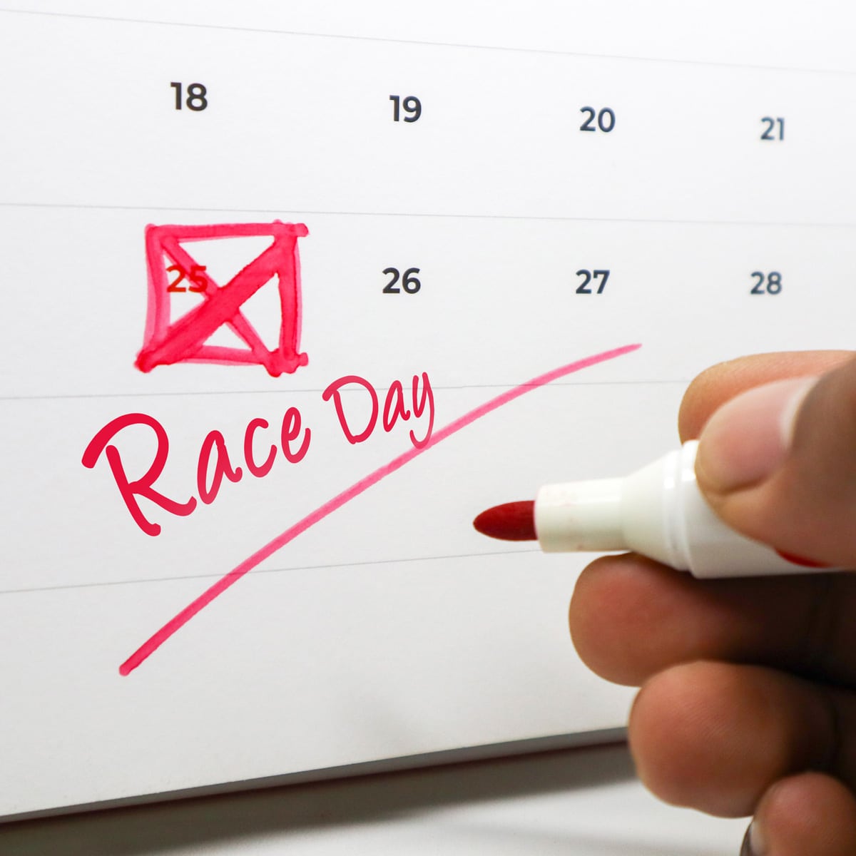 A calendar page with the 25th date boxed and marked in red. Race Day is written in large script below. A hand with a red marker writes on the calendar.