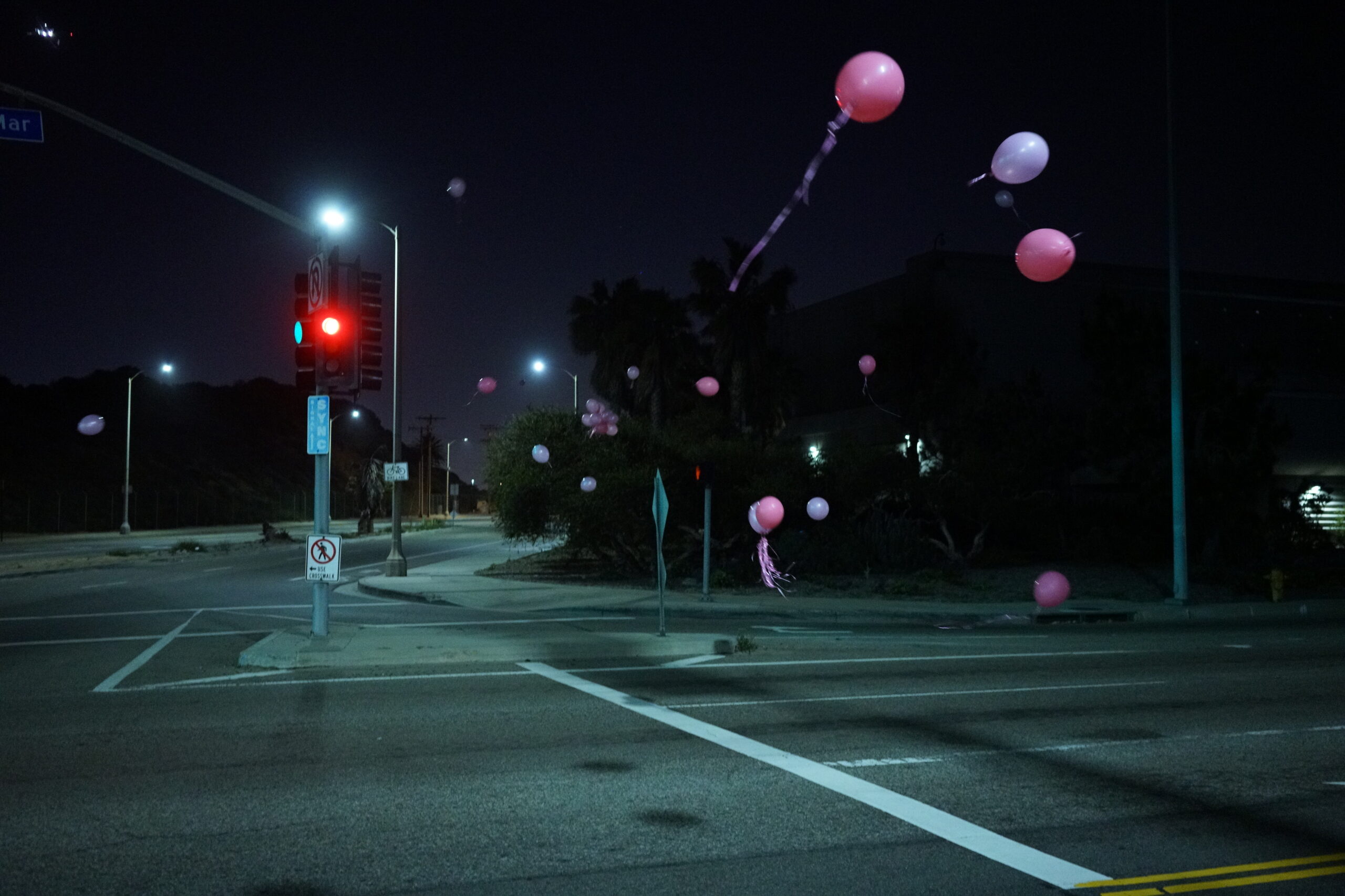 Pink balloons float in the air above a deserted city street near Los Angeles International Airport at 1:06am, illuminated by streetlights and a red traffic signal, moments after Andy Funk departed Dockweiler Beach for the first-ever 365-mile Vegas In 24 ultra-cycling attempt.