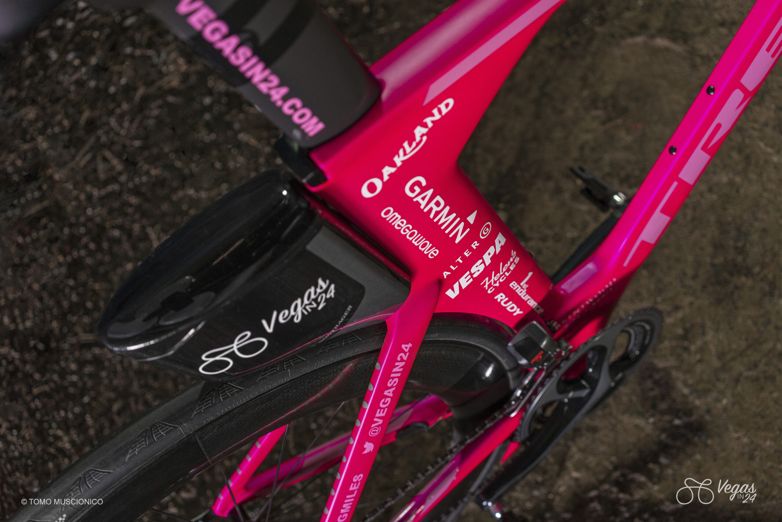 Close-up of the official Vegas In 24 all-pink Trek Speed Concept with various sponsor logos, including Garmin, Trek, Rudy Project, 1st Endurance and others. Photographed from above on a dark surface during the week prior to the completion of the first-ever Vegas In 24 ultra-cycling challenge.