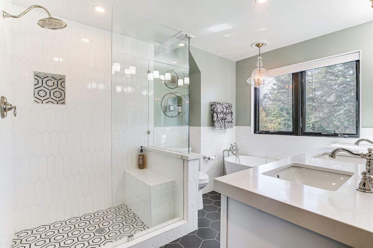 Modern bathroom with a glass shower, built-in bench, hexagonal tile accents, double sinks, and a freestanding tub—designed to reflect the bright, clean style found in luxury athlete accommodations in Lake Arrowhead during the Ho'Omau Altitude Haus training camp.