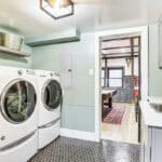 Modern laundry room with a front-loading washer and dryer, gray cabinets, a black faucet sink, and hexagonal tile flooring—showcasing the luxury athlete accommodations found in Lake Arrowhead during the Ho'Omau Altitude Haus training camp.