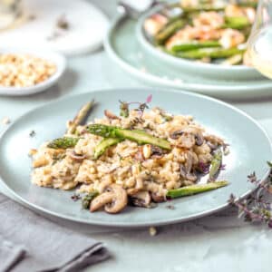 A plate of farro mushroom risotto with asparagus is served on a table next to a glass of white wine. The image showcases Race-Ready Kitchen's Farro Funghi Recovery Risotto for mitochondrial repair and muscle relaxation.