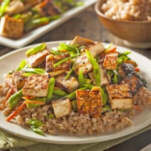 A plate of tofu stir-fry and grains sits on a table, fresh from the Race-Ready Kitchen. The tofu is golden and crispy, garnished with sliced green onions.