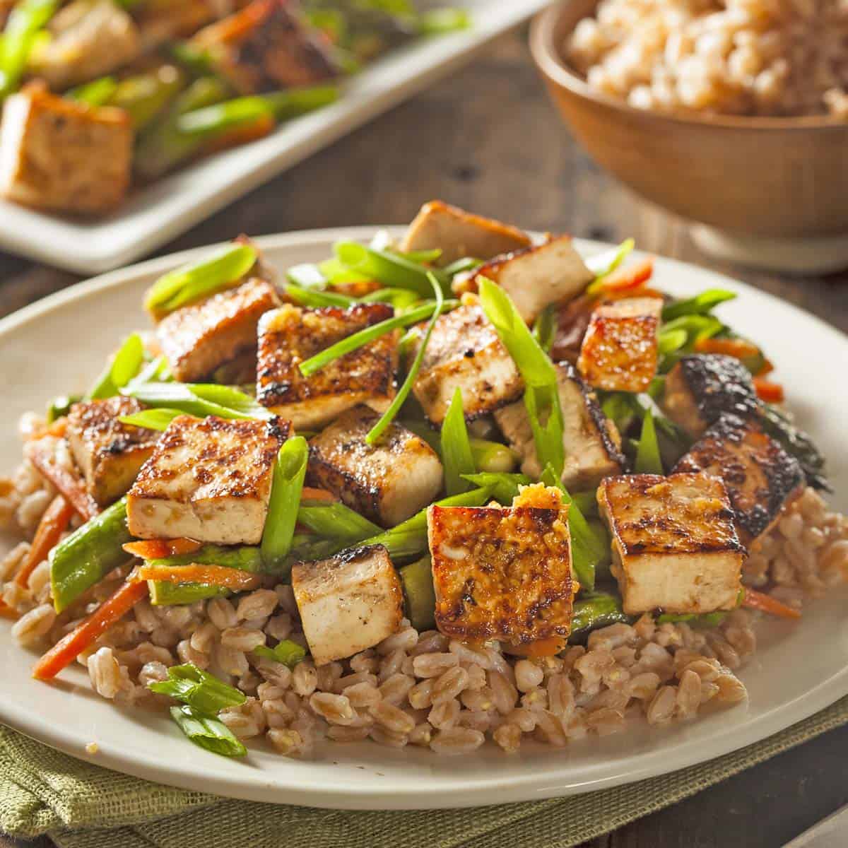 A plate of tofu stir-fry and grains sits on a table, fresh from the Race-Ready Kitchen. The tofu is golden and crispy, garnished with sliced green onions.